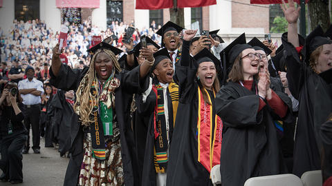 Students in cap and gowns cheer at the end of Commencement 2025.