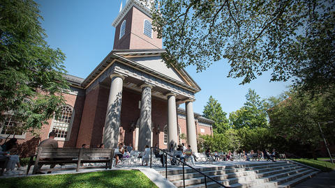 Students relax at tables on the porch of the Memorial Church on a sunny day.