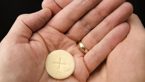 Open hands hold a communion wafer with a cross in the center.