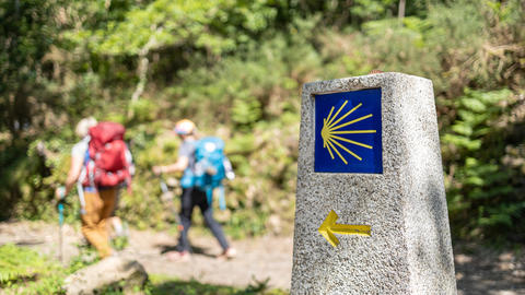 Hikers walk past a stone marker on the Camino de Santiago.