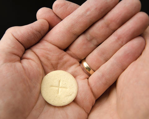 Open hands hold a communion wafer with a cross in the center.
