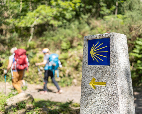 Hikers walk past a stone marker on the Camino de Santiago.