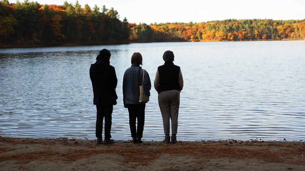 Professor Stephanie Paulsell and two students stand on the shore of Walden Pond
